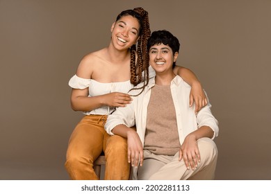 Portrait Of A Multiracial Woman In Her 20's And A Punjabi Person In Their 20's Smiling On A Neutral Background.