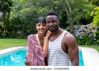 Portrait Of Multiracial Young Couple Standing By Swimming Pool In Backyard. Unaltered, Togetherness, Lifestyle, Leisure, Bonding, Weekend Activities.