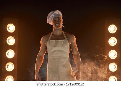 Portrait Of Muscular Chef Wearing White Apron And Cheef Hat, Posing On Smoky Background Male Housewife. Husband In Kitchen. Brutal Butcher.