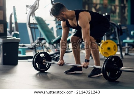 Portrait Of Muscular Middle Eastern Guy Making Deadlift Workout At Modern Gym, Young Arab Male Athlete Lifting Heavy Barbell At Sport Club Interior, Training Muscle Endurance, Closeup Shot