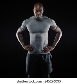 Portrait Of Muscular Young Man In Sportswear Standing With His Hands On Hips Against Black Background. Strong African Athlete.