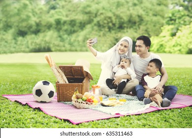 Portrait Of Muslim Family Using A Mobile Phone To Take A Picture Together While Picnicking In The Park