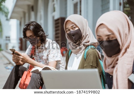 Portrait muslim wearing masks female students looking at the camera. with busy friends in the background