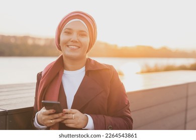 Portrait muslim woman wearing hijab using mobile phone outdoor. Arabic woman wearing headscarf using smartphone on street. Islamic girl texting a message phone in city centre. - Powered by Shutterstock