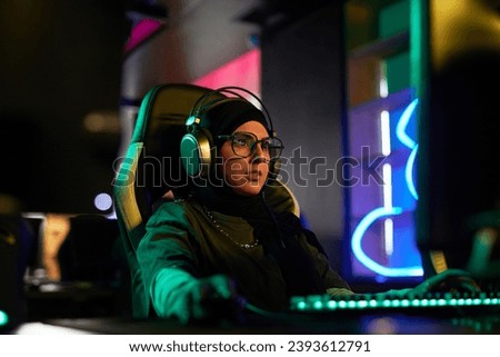 Portrait of Muslim young woman playing videogames in neon light and wearing headphones, cyberpunk style