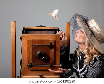 Portrait of a mysterious beautiful young woman in a hat and dress with long sleeves looking at a bird on a gray background. Retro style and vintage concept. Advertising space