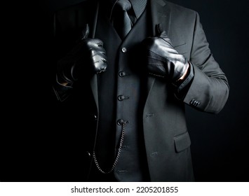 Portrait Of Mysterious Man In Dark Suit And Leather Gloves Standing Proudly On Black Background. Concept Of Mafia Hitman Or Hotel Concierge.