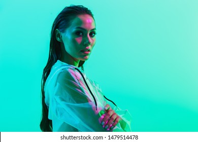 Portrait of naked gorgeous serious woman posing isolated over blue wall background with neon bright lights dressed in raincoat.