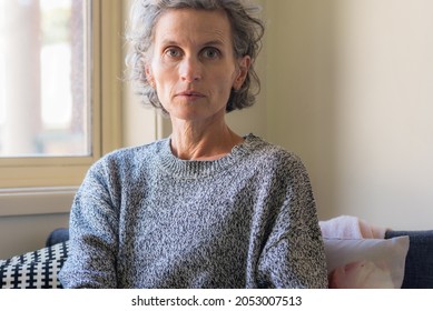 Portrait of natural looking middle aged woman with grey hair next to window (selective focus)