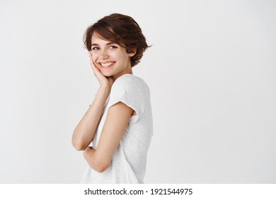 Portrait Of Natural Young Woman With Short Hair, Touching Pure Clean Skin And Smiling, Standing Against White Background. Copy Space