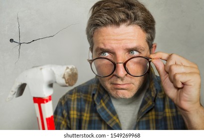 Portrait Of Nerd Man Looking To Hammer After Driving A Nail For Hanging A Frame Making Funny Face For The  Mess Cracking The Wall As A Disaster DIY Guy And Messy Domestic Repair Task At Home