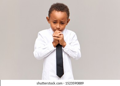 Portrait of nervous frustrated sad African American schoolboy in uniform looking down with worried facial expression, gnawing nails, scared of being told off for bad marks at school. Sincere emotions - Powered by Shutterstock