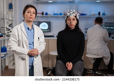 Portrait Of Neurologist Doctor Standing Beside Woman Patient With Medical Eeg Headset During Neuroscience Experiment In Medical Laboratory. Team Of Researcher Analyzing Brain Activity Evolution