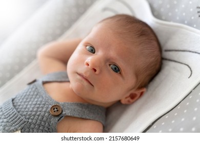 Portrait Of A Newborn Baby In Bed Looking At The Camera.