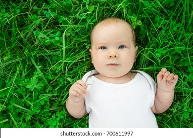 Portrait Of A Newborn Baby With Blue Eyes Lying On Green Grass And Looking Up Closeup. Girl With Blue Eyes The Top View. Place For Text. The Concept Of Childhood. Earth Day