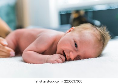 Portrait of newborn baby boy with blond hair having his diaper changed lying on blanket on floor with uncomfortable expression. Horizontal close-up indoor shot. High quality photo - Powered by Shutterstock