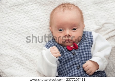 Portrait of a newborn baby wearing an elegant vest with a red bow tie.