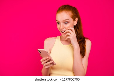 Portrait nice adorable charming cheerful positive dreamy red  haired girl in tanktop and ponytail  reading winning sms in smart  phone  isolated bright vivid fuchsia background