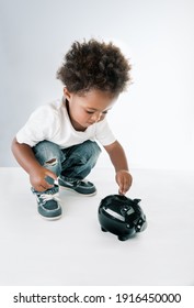 Portrait of a Nice African American Child Putting Coins in to the Pig-shaped Money Box. Isolated on Grey White Background. Hope for Better Future