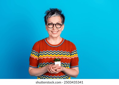 Portrait of nice aged lady hold tiny plant empty space wear t-shirt isolated on blue color background - Powered by Shutterstock