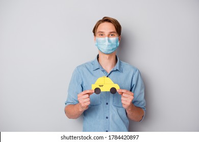 Portrait of  nice attractive guy wearing safety gauze mask holding in hands card car figure taxi service covid prevention social distance isolated over grey color background