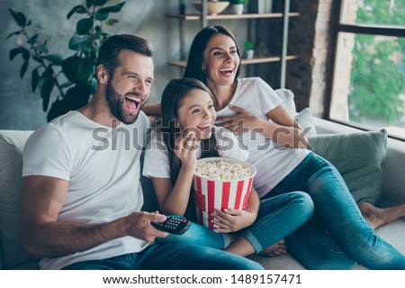 Portrait of nice attractive lovely positive glad cheerful cheery family wearing casual white t-shirts jeans denim sitting on sofa having fun watching funny video enjoying spending free time