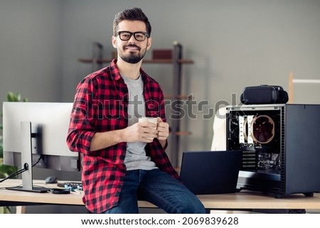 Portrait of nice attractive smart clever cheerful guy sitting on table drinking beverage at work place station indoors