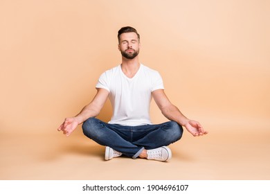 Portrait of nice calm focused guy sitting on floor meditating relaxation isolated over beige pastel color background