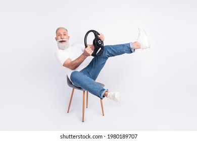 Portrait Of Nice Comic Cheerful Man Sitting On Chair Holding Steering Wheel Driving Invisible Car Fooling Isolated Over Grey Color Background