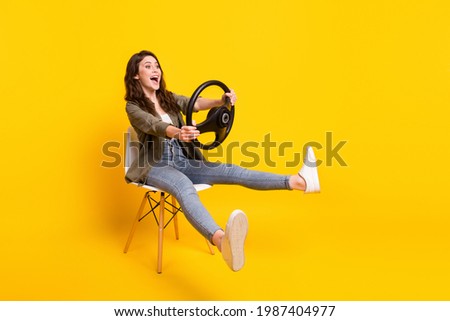 Portrait of nice funny cheerful girl sitting on chair holding steering wheel riding fooling isolated over bright yellow color background