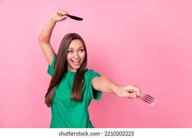 Portrait of nice positive funny girl long hairstyle wear green t-shirt hold fork knife look empty space isolated on pink color background