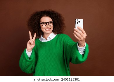 Portrait of nice positive girl hold smart phone make selfie demonstrate v-sign isolated on brown color background