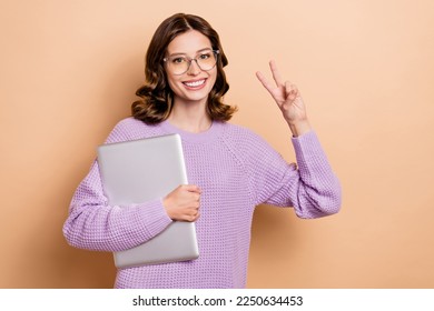 Portrait of nice pretty cheerful girl with wavy hairstyle wear violet pullover hold laptop show v-sign isolated on pastel color background
