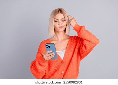 Portrait of nice young girl ponder use phone orange cardigan isolated on grey color background - Powered by Shutterstock