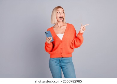 Portrait of nice young girl smart phone indicate finger empty space orange cardigan isolated on grey color background - Powered by Shutterstock