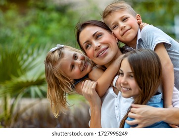 Portrait Of A Nice Young Mother With Pleasure Spending Time With Her Three Precious Kids In The Spring Park, Everyone Hugging Their Lovely Mom, Having Fun Together, Happy Big Family Enjoying Life