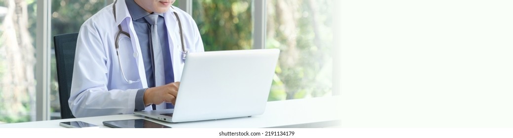 Portrait Of No Face Asian Senior Doctor Sitting In Medical Office While Using Laptop Computer. Banner Ratio 4:1