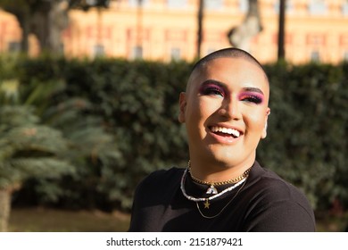 Portrait of non-binary person, young and South American, heavily make up, smiling happily, getting sun rays on face. Concept queen, lgbtq+, pride, queer.