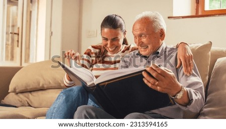 Portrait of a Nostalgic Woman Bringing the Family Photo Album to her Senior Father so They Can Watch Photos Together. Old Man Sharing Memories and Stories with his Daughter in a Bonding Moment