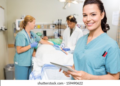 Portrait of nurse with digital tablet while doctor and colleague operating male patient in hospital