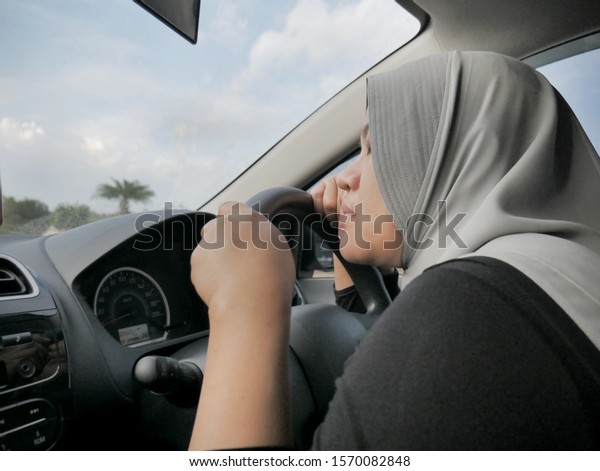 Portrait o Asian muslim lady\
slept in her car, tired in the trip, taking nap by the side of the\
road