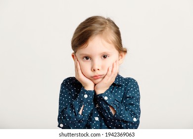 Portrait Of An Offended, Gloomy, Angry Little Girl 4-6 Years Old Wearing A Blue Dress With Polka Dots. Cute Sad Kid Girl On A White Background