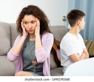 Portrait Of Offended Mother After Disagreements With Teenager Son Sitting At Home