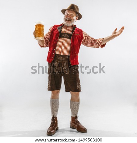 Portrait of Oktoberfest senior man in hat, wearing the traditional Bavarian clothes. Male full-length shot at studio on white background. The celebration, holidays, festival concept. Drinking beer.
