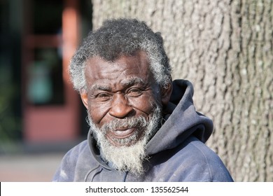 Portrait Of Old African American Homeless Man In Black In White Outdoors.