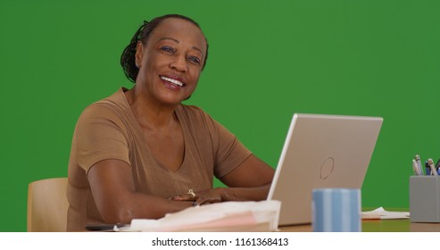 Portrait Of Old Black Woman Sitting At Desk With Laptop Smiling On Green Screen