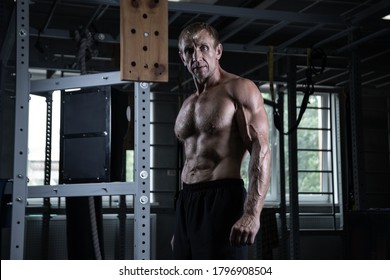 Portrait of an old brutal bodybuilder with a serious face posing in the gym. Muscular adult male with naked torso