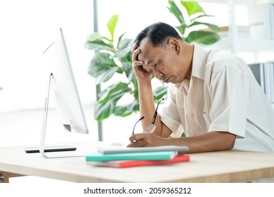 Portrait Of An Old Elderly Asian Man Holds The Head With His Hand Cause Of Stress After Try To Use A Computer Laptop After Retired. Concept Of Ageism And Hobbies After Retirement.