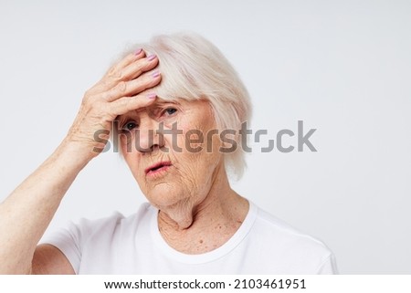Portrait of an old friendly woman holding his head discontent problem light background
