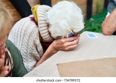 Portrait Of Old Lady Laughing Hysterically Hiding Her Face While Playing Card Game With Friends Outdoors